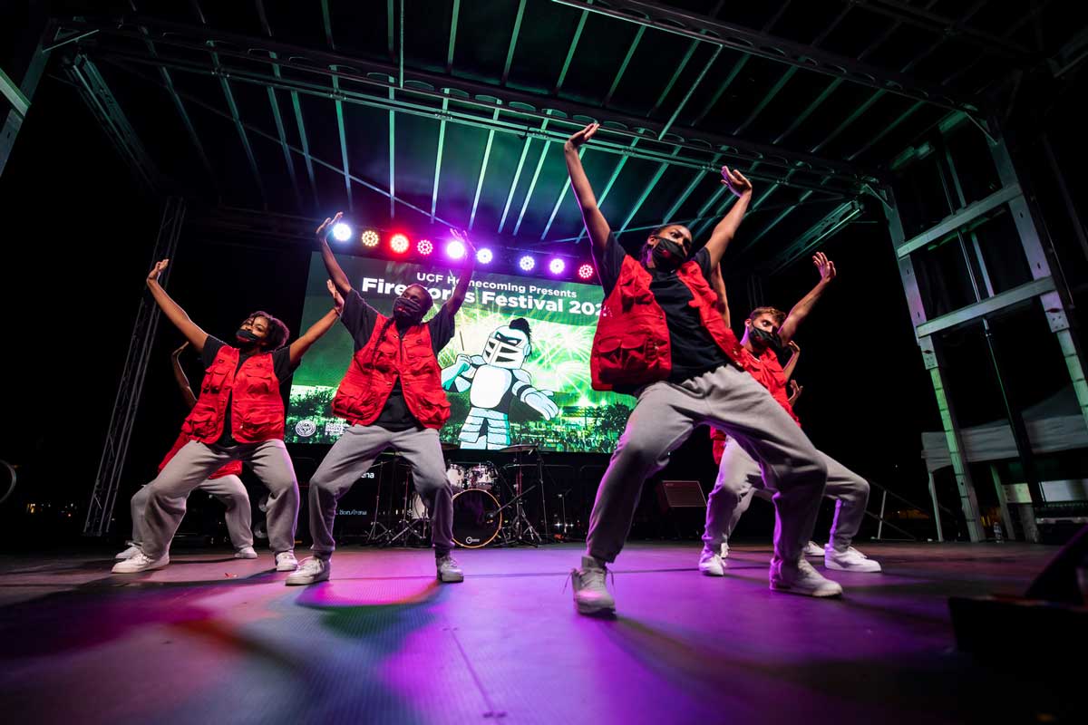 Dancers wearing red vests perform on stage