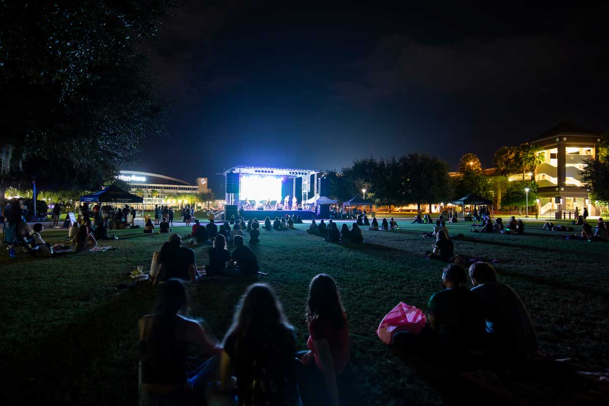 groups of people sit on Memory Mall with stage lit up at night