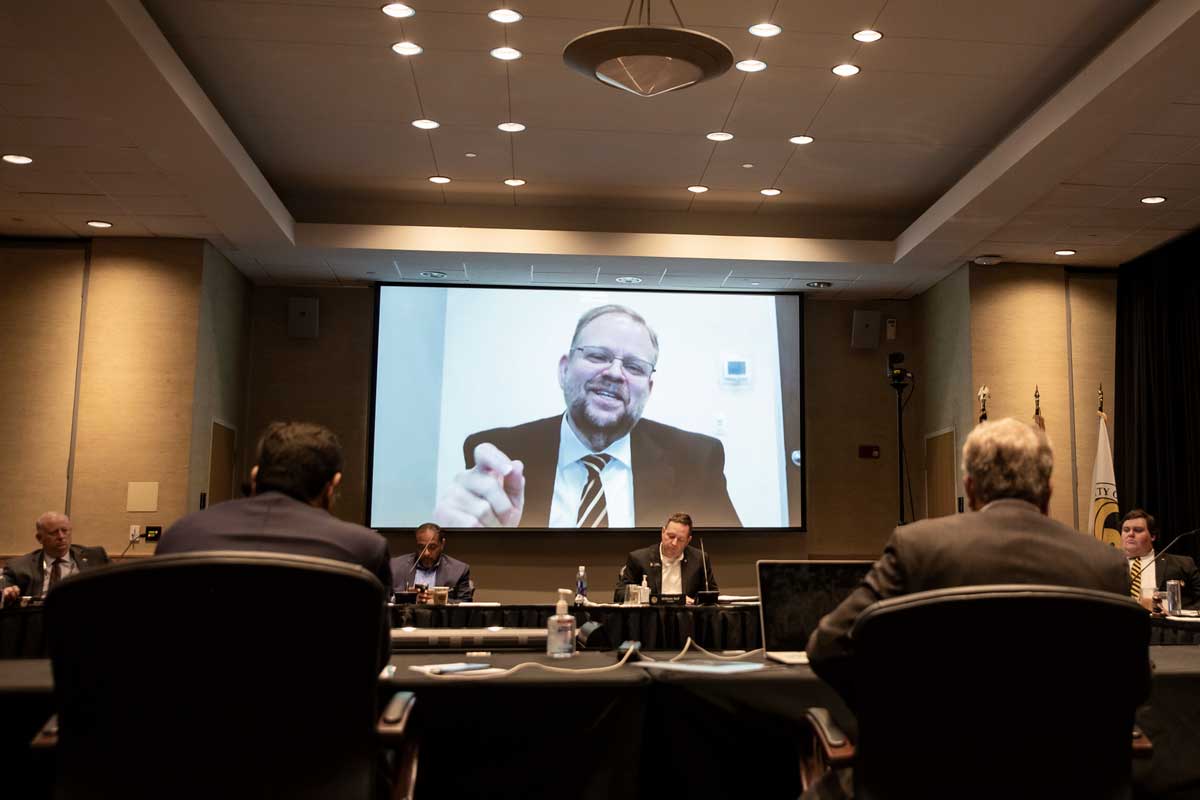 Alexander N. Cartwright addresses conference room from large video screen