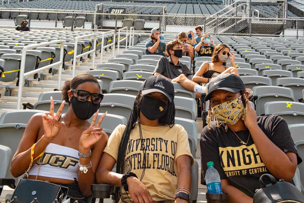 Three Black women wearing Knights T shirts pose for a photo in their seats at the Bounce House