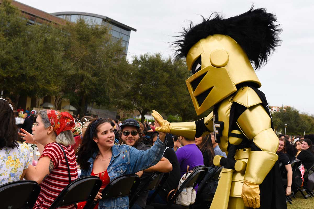 Knightro high fives student seated at a table on Memory Mall