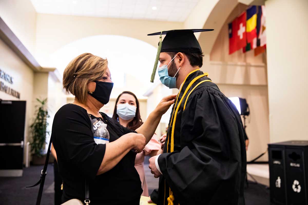 A blonde woman straightens her son's cap and gown