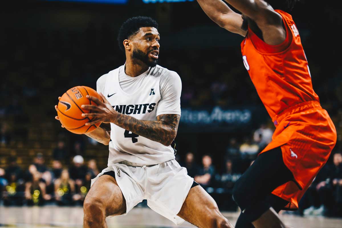 Men's basketball player in white uniform is guarded by SMU defender in red uniform