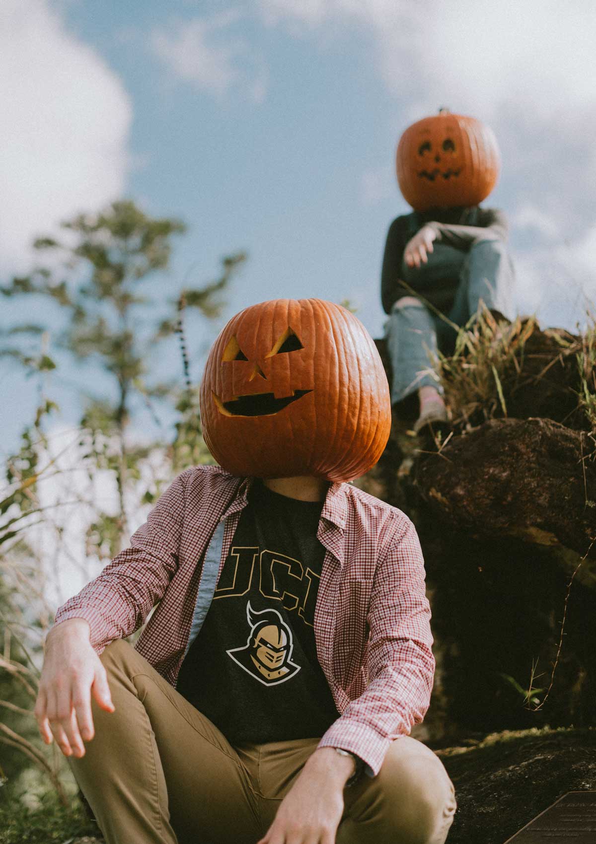 Two humans wearing jack-o-lanterns sit outside