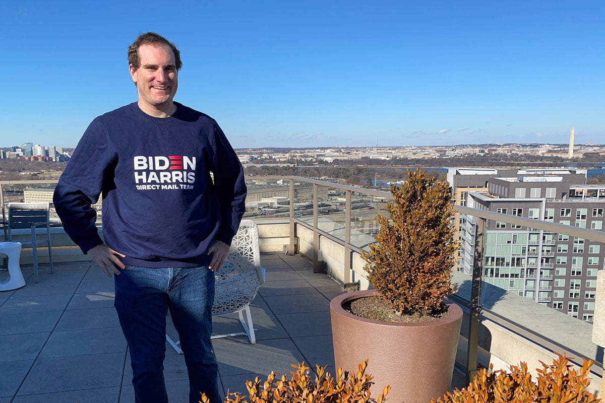 David Mariutto wears a Biden Harris sweatshirt and poses with the Washington Monument in the background