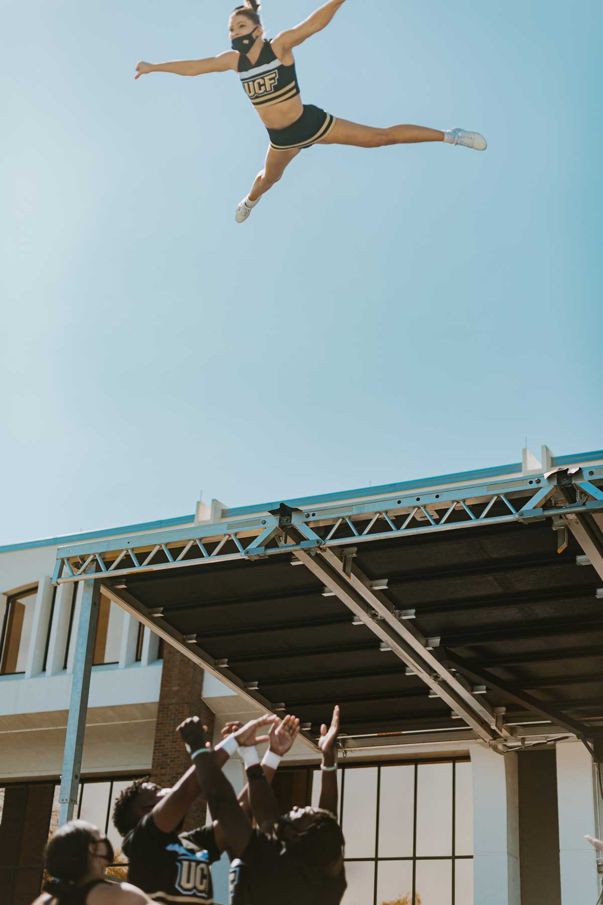 Female cheerleader soars in the sky while base cheerleaders prepare to catch her.