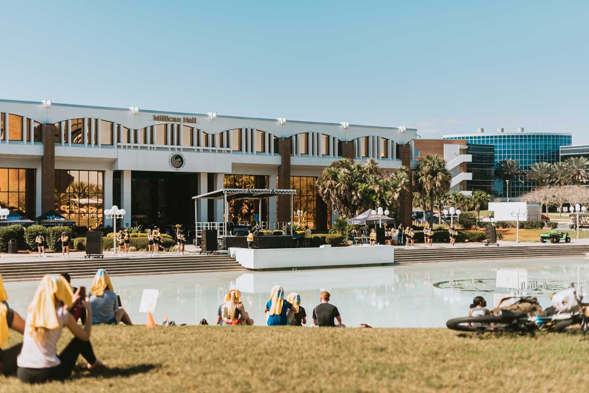 Students sit on lawn near Reflecting Pond with Millican Hall in the background