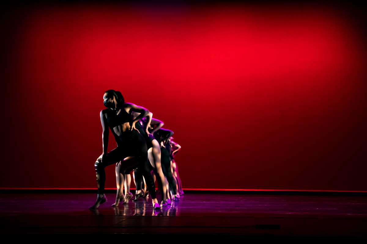 Dancers form a stacked line on stage with a red backdrop