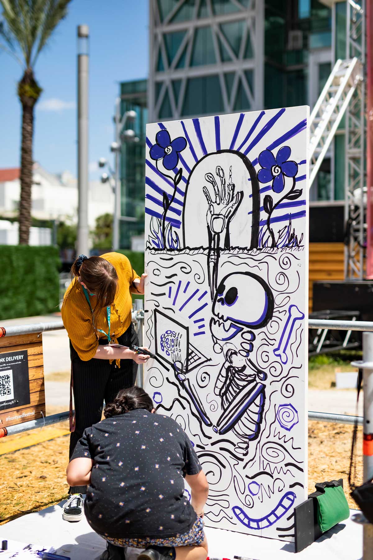 Two students paint on canvas a skeleton reaching up one hand, and reading with the other