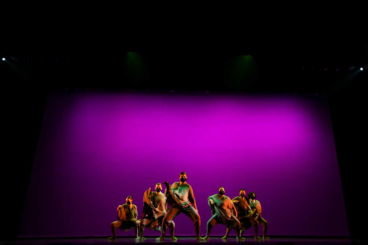 Dancers form V on stage with purple background