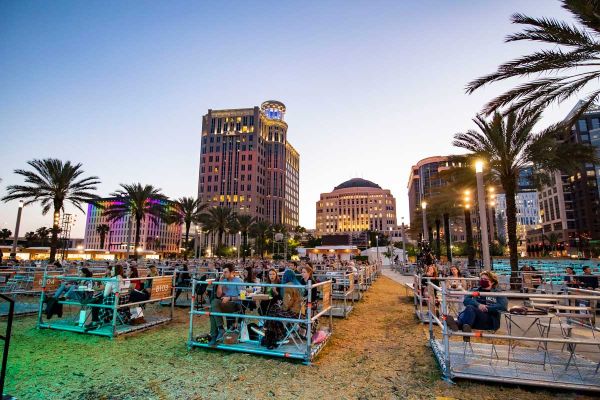 socially distanced crowd separated into structured pods set up on lawn in front of downtown Orlando buildings at sunset