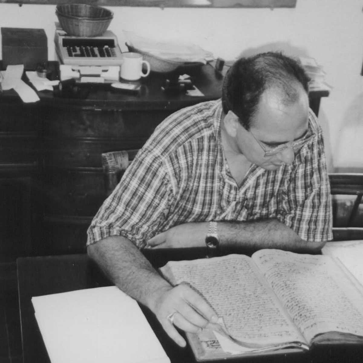 Black and white photo of Luis Martinez-Fernandez sitting at a desk reading over a book