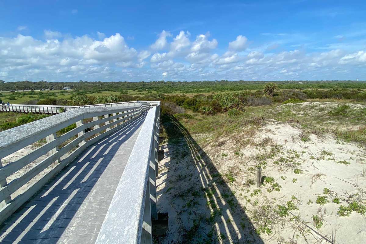 white boardwalk in between sand dunes leads to beach on sunny day