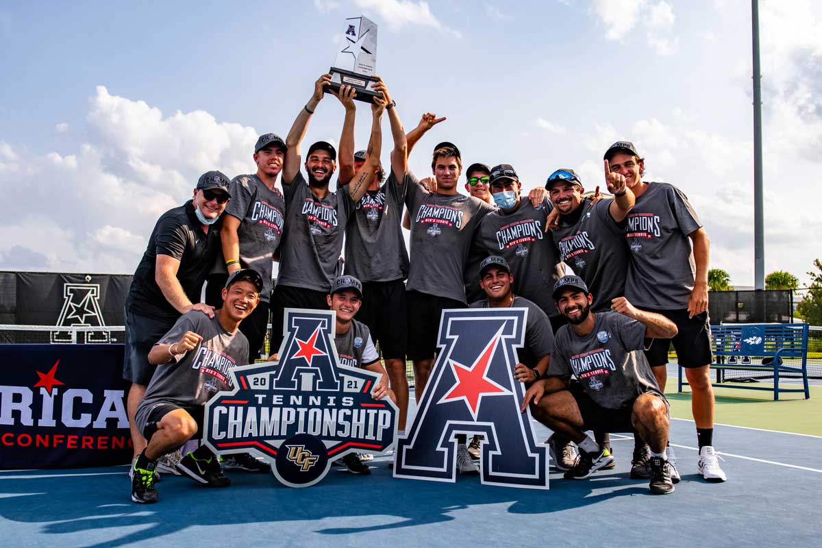 men's tennis team holds AAC Champion signs and trophy on court