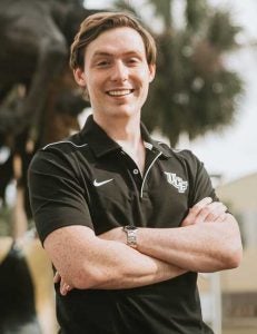 Alex Cumming wears UCF poloshirt and stand with arms crossed