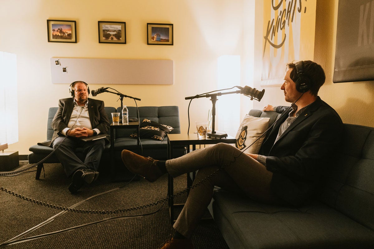 President Alexander Cartwright and host Alex Cumming sit on couches during recording session