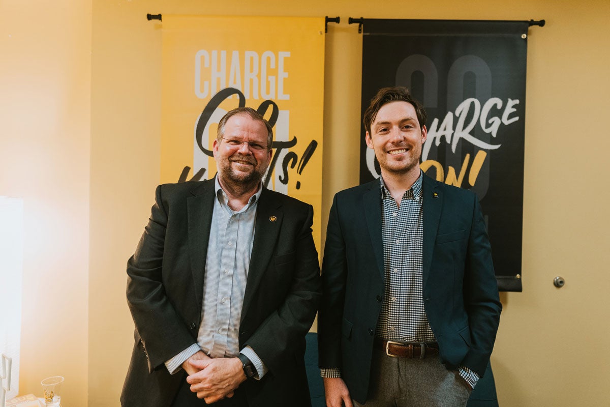 Alexander Cartwright and Alex Cumming stand in front of Go Knights Charge On banners