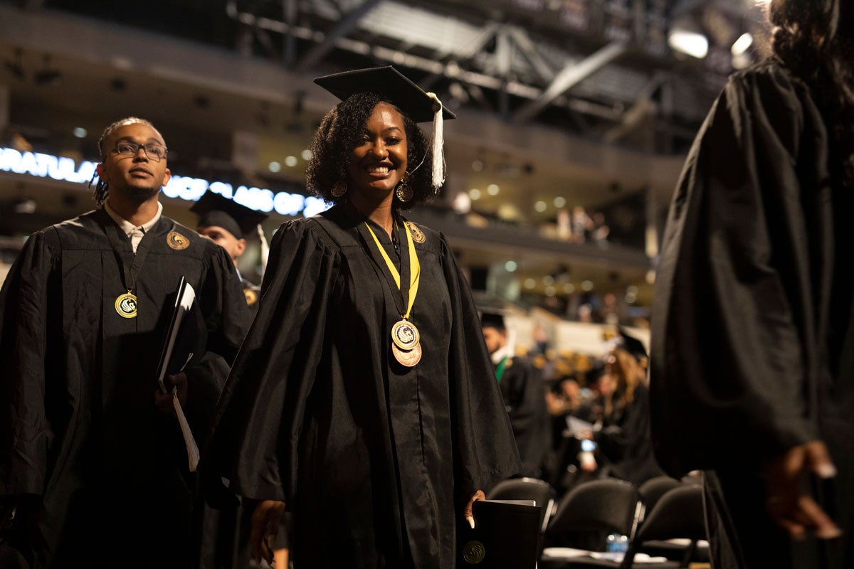 Black woman student in cap and gown smiles at the camera