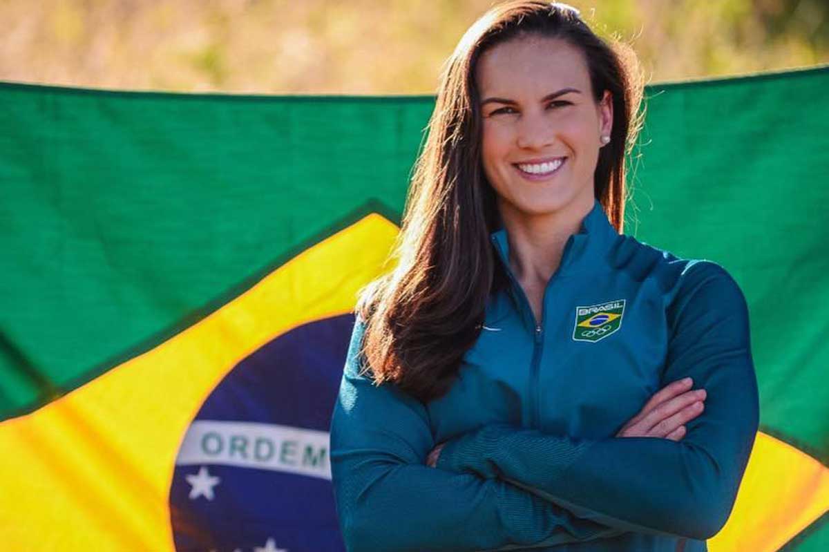 Aline Reis stands with arms crossed in front of Brazilian flag