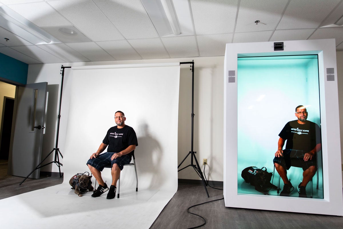 Man sits on a chair on a backdrop with hologram technology next to him to show a side by side comparison