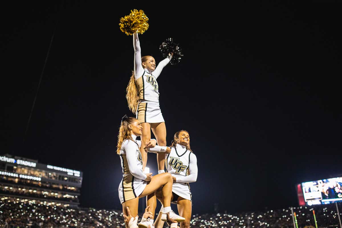 Cheerleaders in stunt form at night time with stadium lights bright behind them