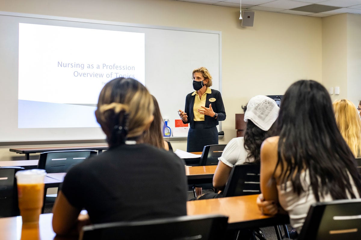 Professor stands at front of a classroom addressing students seated at desks