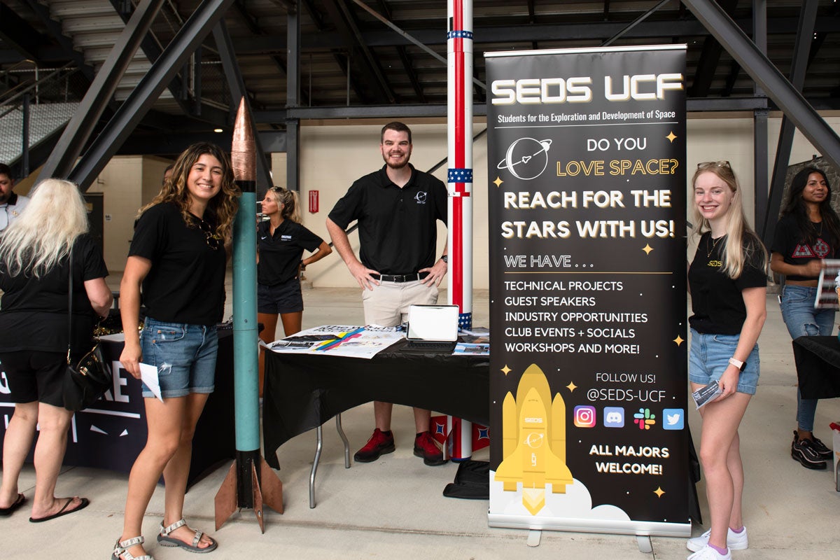 Three students pose with SEOS UCF banner and table 