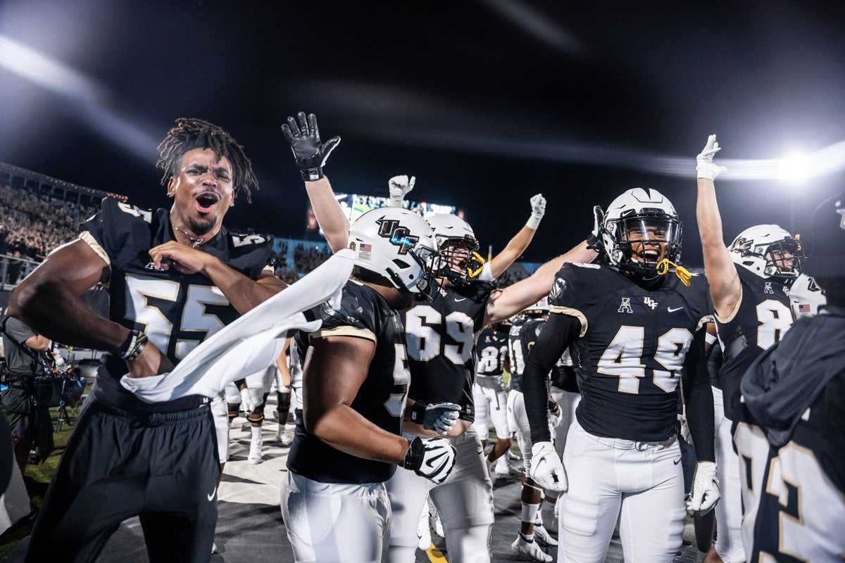 A group of football players cheer on the sidelines