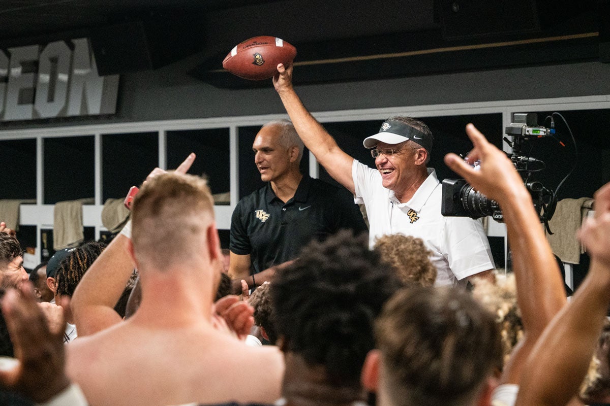 Gus Malzahn holds up a football in celebration with Terry Mohajir standing next to him in locker room