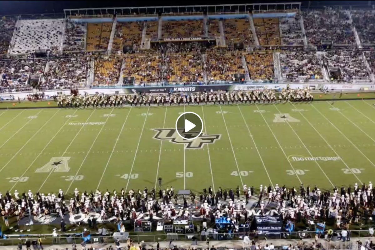 Screen shot of football field with bands on the sidelines and a play button in the middle