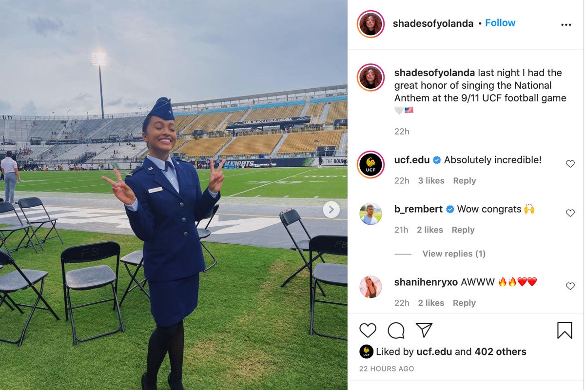 Young woman in air force blue uniform poses on sideline of football field