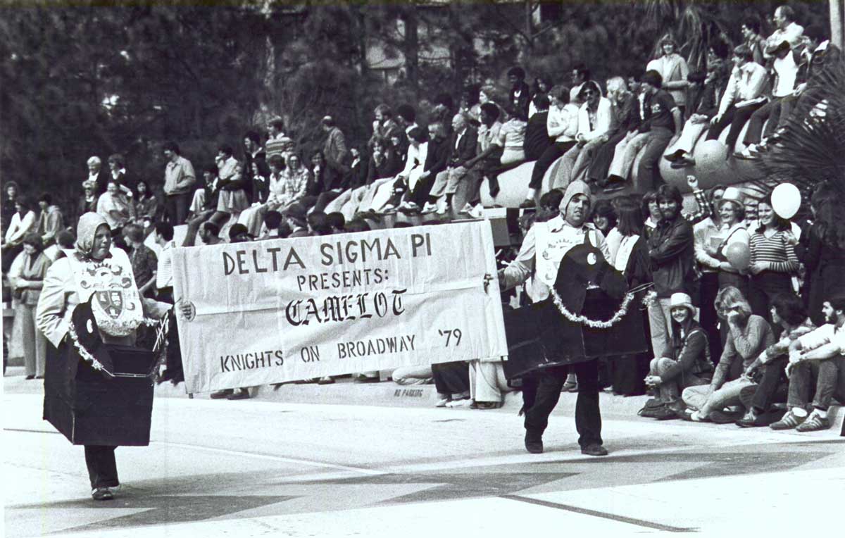 Black and white photo of two men dressed as medieval knights holding banner on parade route 