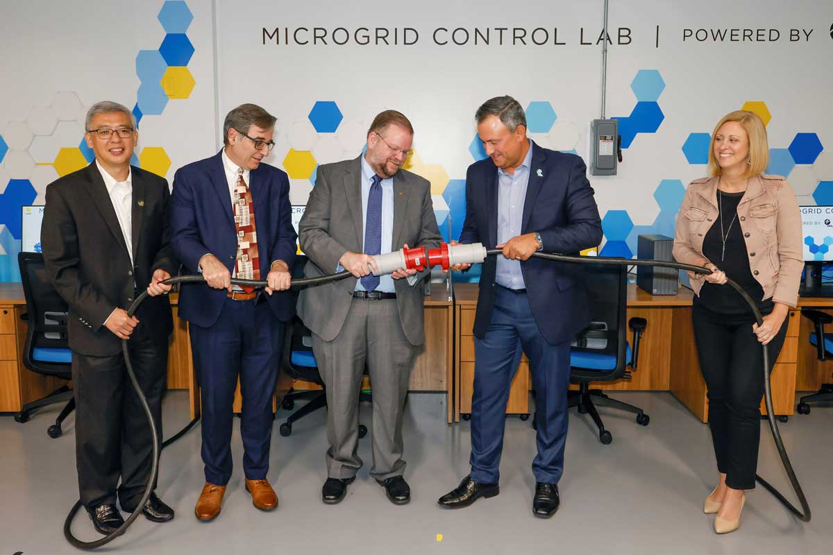 Four men and one woman hold large ceremonial power cord for plug-in ceremony at the Microgrid Control Lab