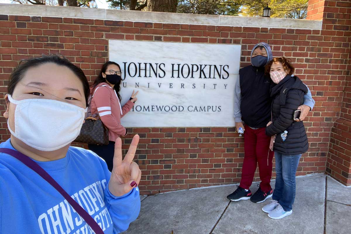 Sharon Park poses with her sister and parents in front of brick wall with Johns Hopkins sign