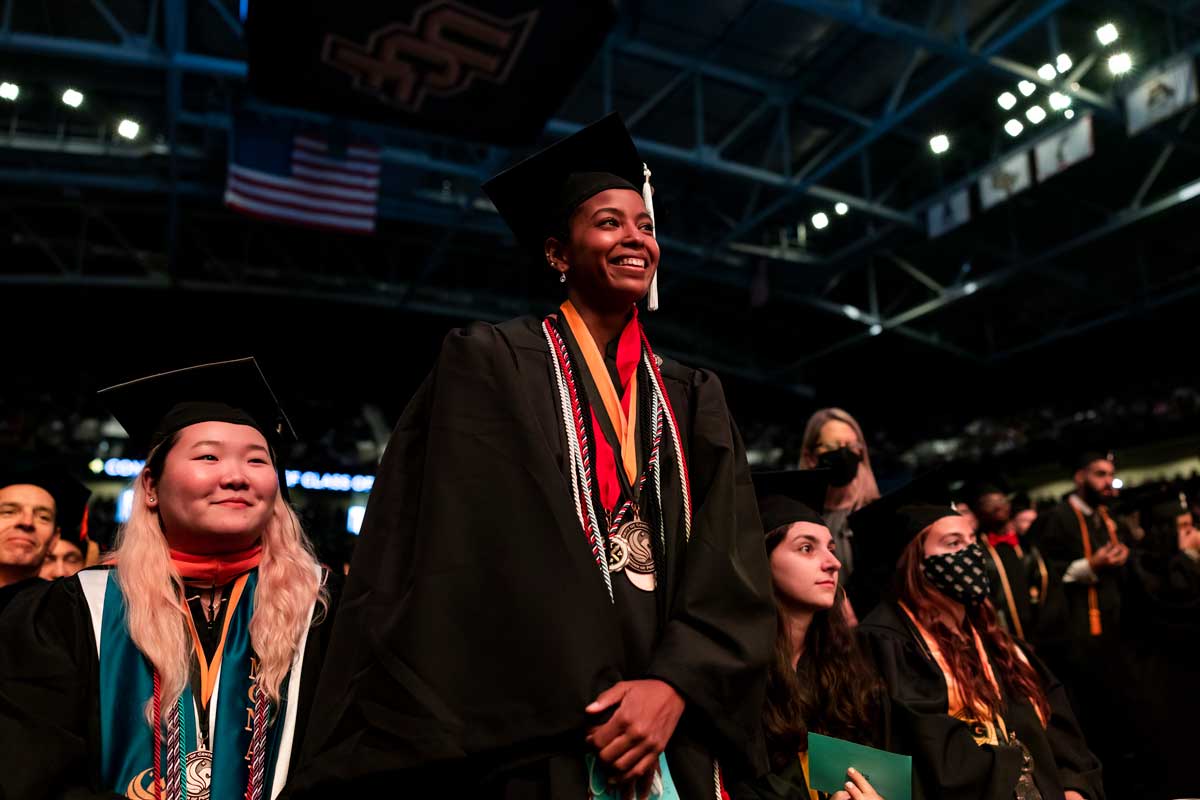 Black woman stands proudly in cap and gown during commencement ceremony