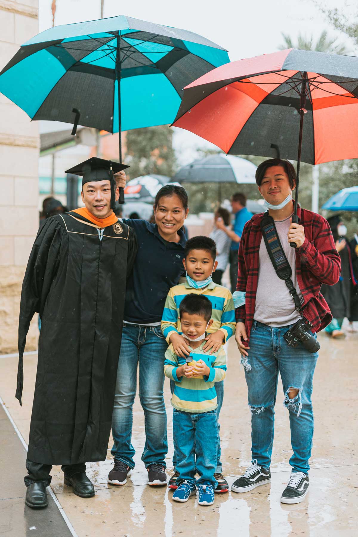 A PhD graduate and his family hold two umbrellas and smile