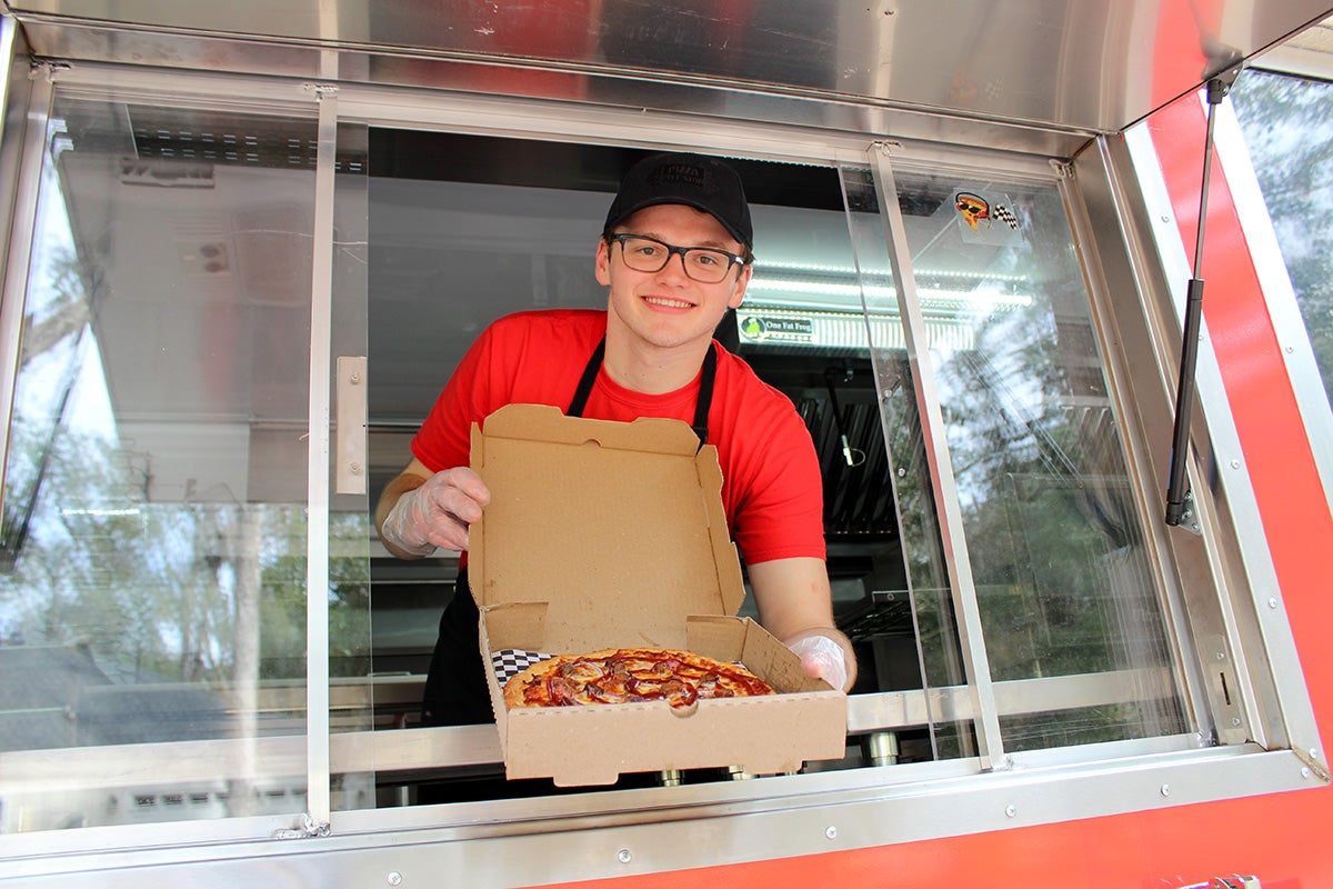 UCF Rosen College graduate and founder of Pizza Pitt Stop Dylan Pittman opening box of pepperoni pizza