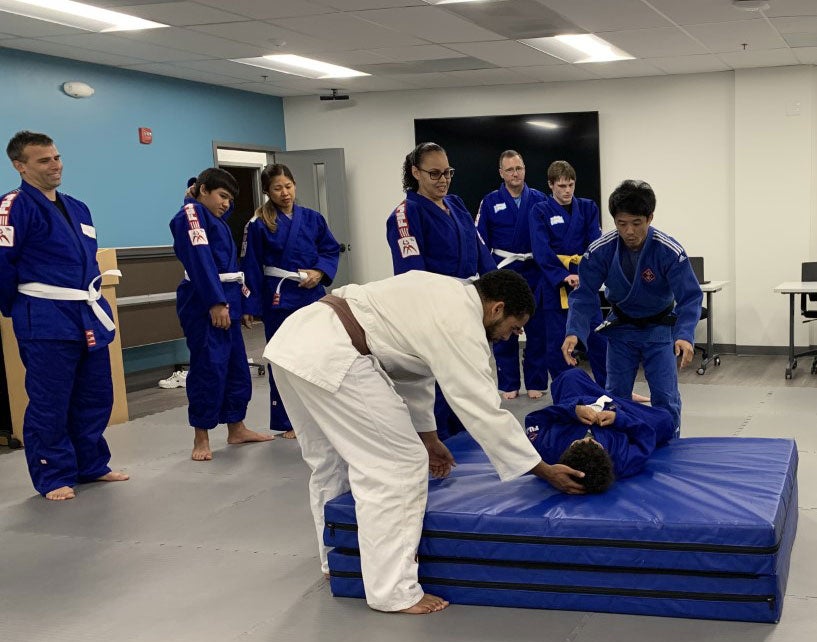 A judo instructor performs a demonstration in a room full of participants.