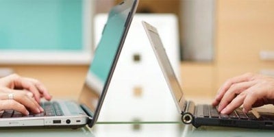 sideview of two open laptops and people typing on them