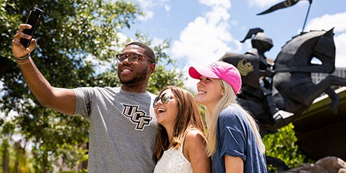 group of ucf students taking a selfie in front of a statue of a knight on horse