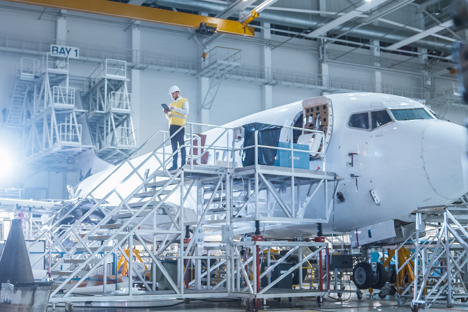 Aerospace engineer in safety vest holds tablet next to an airplane.