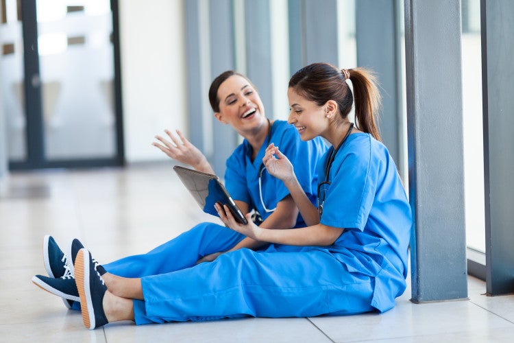 Two nurses using a tablet while sitting on the ground