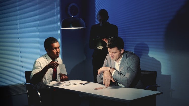 A police detective questions a suspect in an interrogation room.