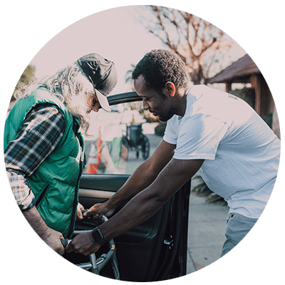 Young man helping older man out of a car.