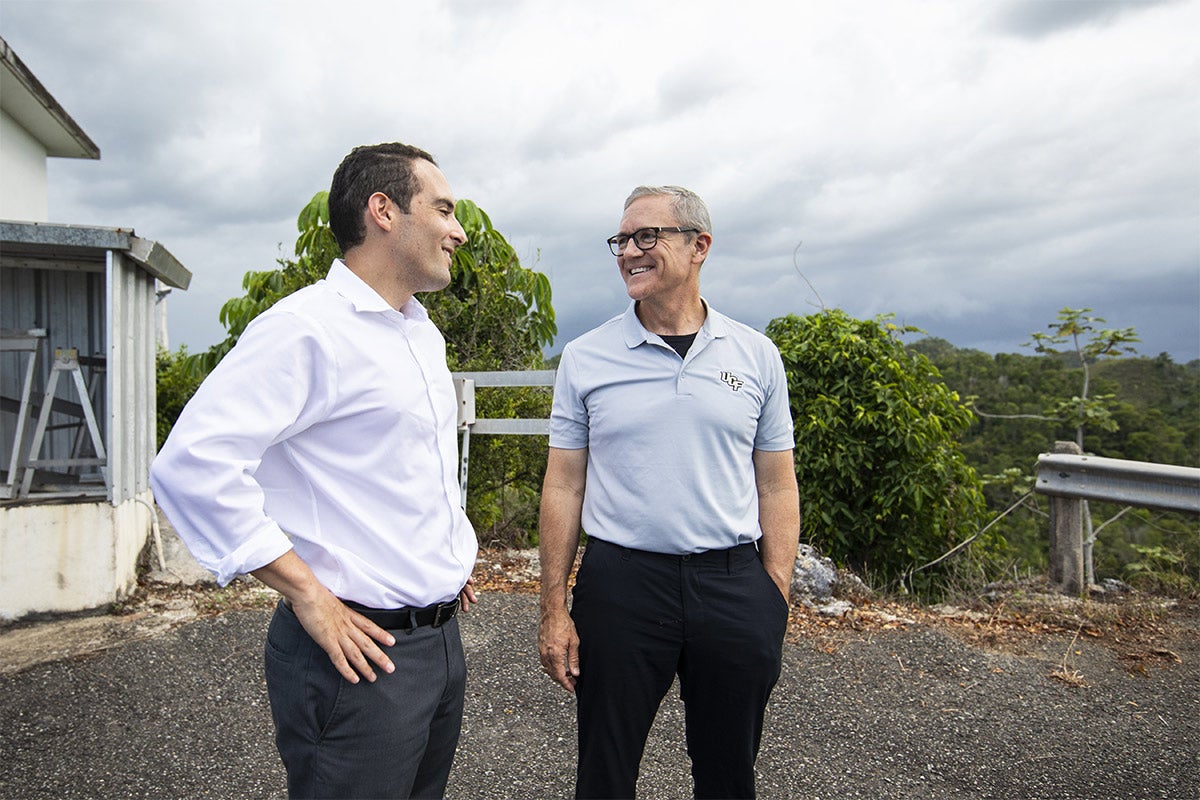 President Dale Whittaker wearing grey UCF polo, black pants and glasses, smiling at man with white shirt, grey pants, and his hands on his hips at Arecibo. President Dale Whittaker wearing grey UCF polo, black pants and glasses, smiling at man with white shirt, grey pants, and his hands on his hips at Arecibo.