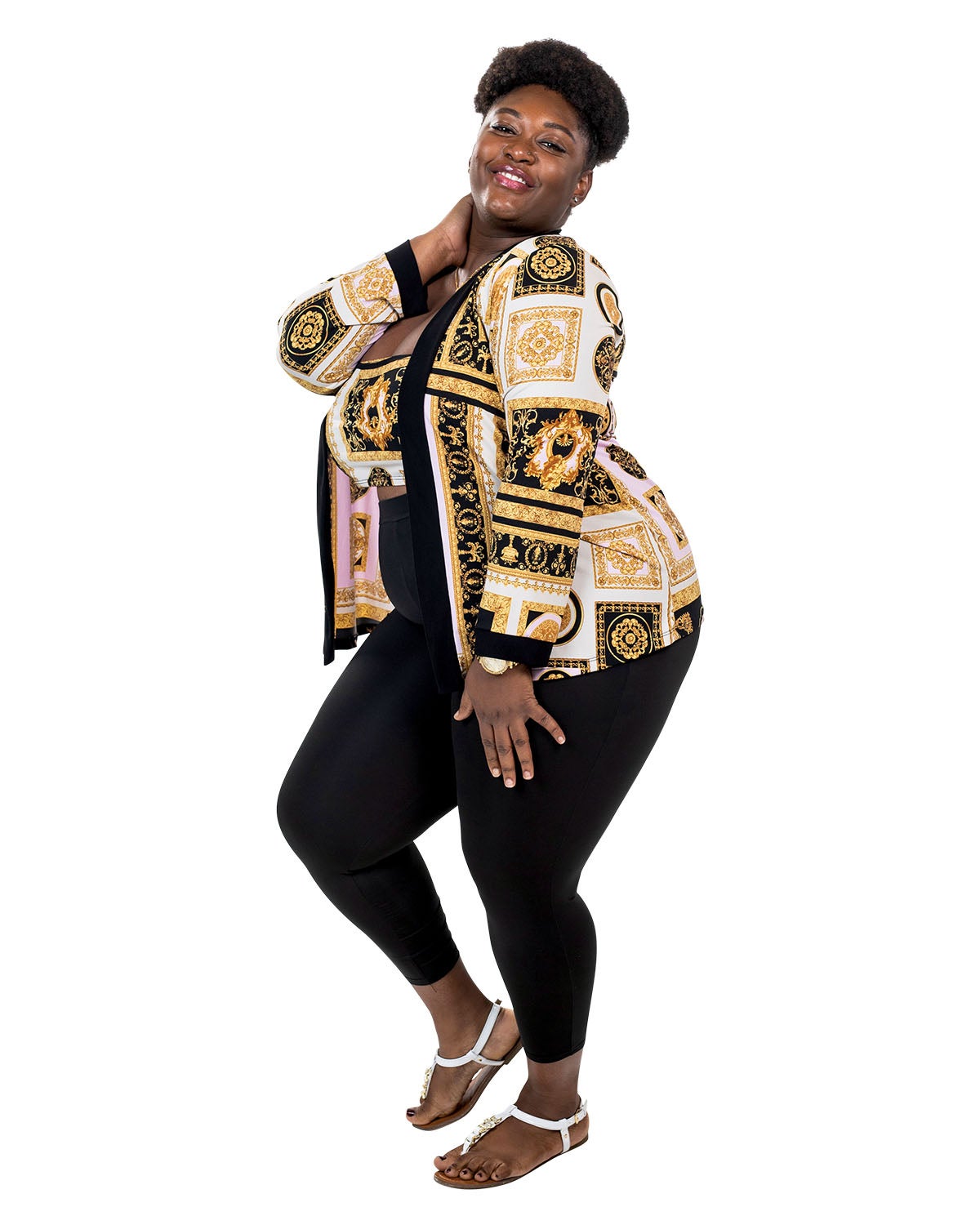 A woman in an ornate jacket and top, and black leggings, poses with her hands on her neck and leg as she smiles. A woman in an ornate jacket and top, and black leggings, poses with her hands on her neck and leg as she smiles.