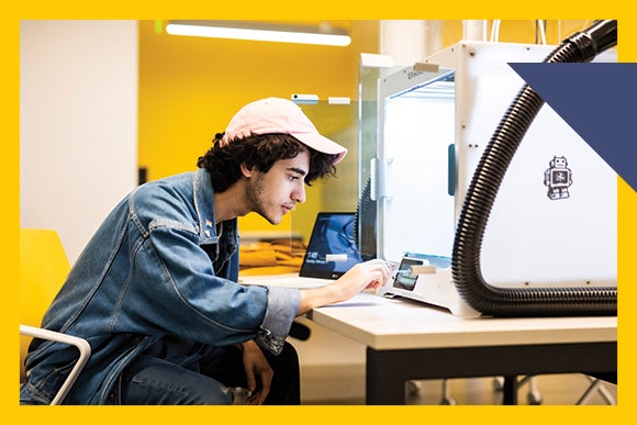 Male student wearing denim jacket and pink ball cap leans in to white box machine