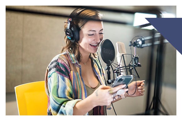 Woman in sound booth wears head phones and speaks into microphone