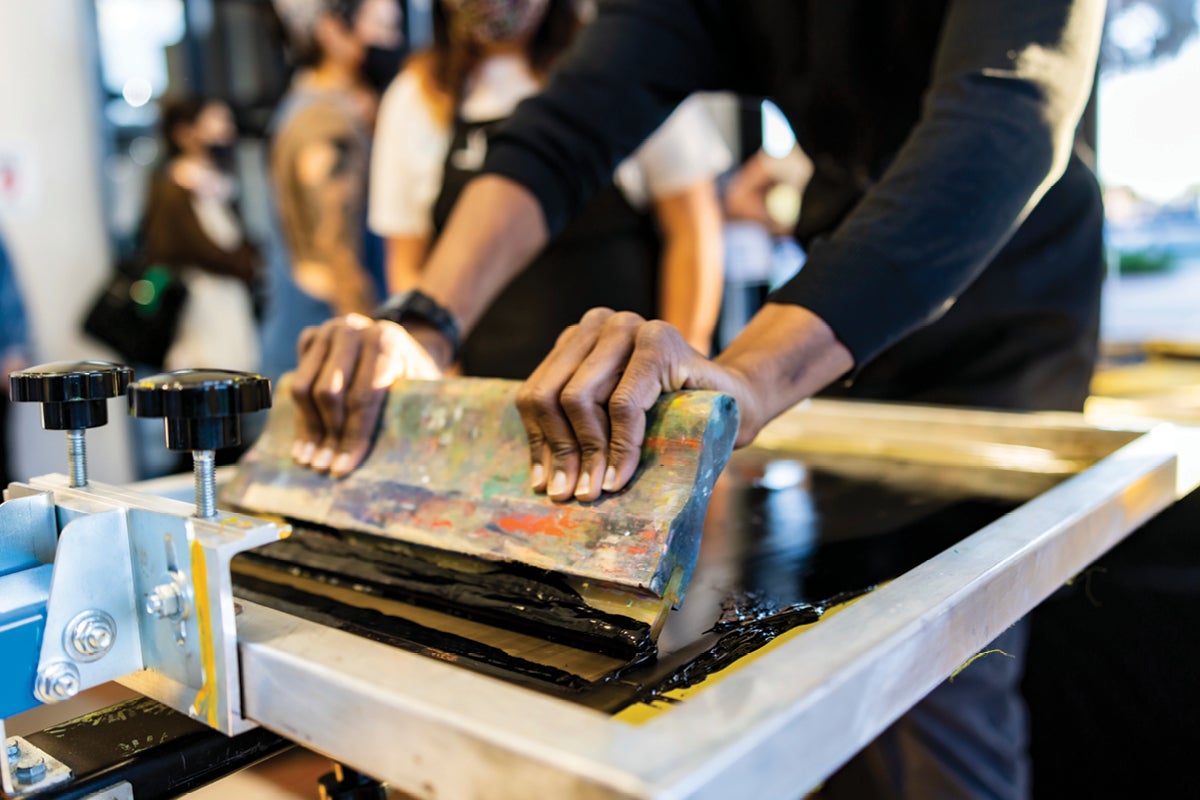 A closeup shot of a person's hands pulling the squeegee of a screen-printing mesh screen.