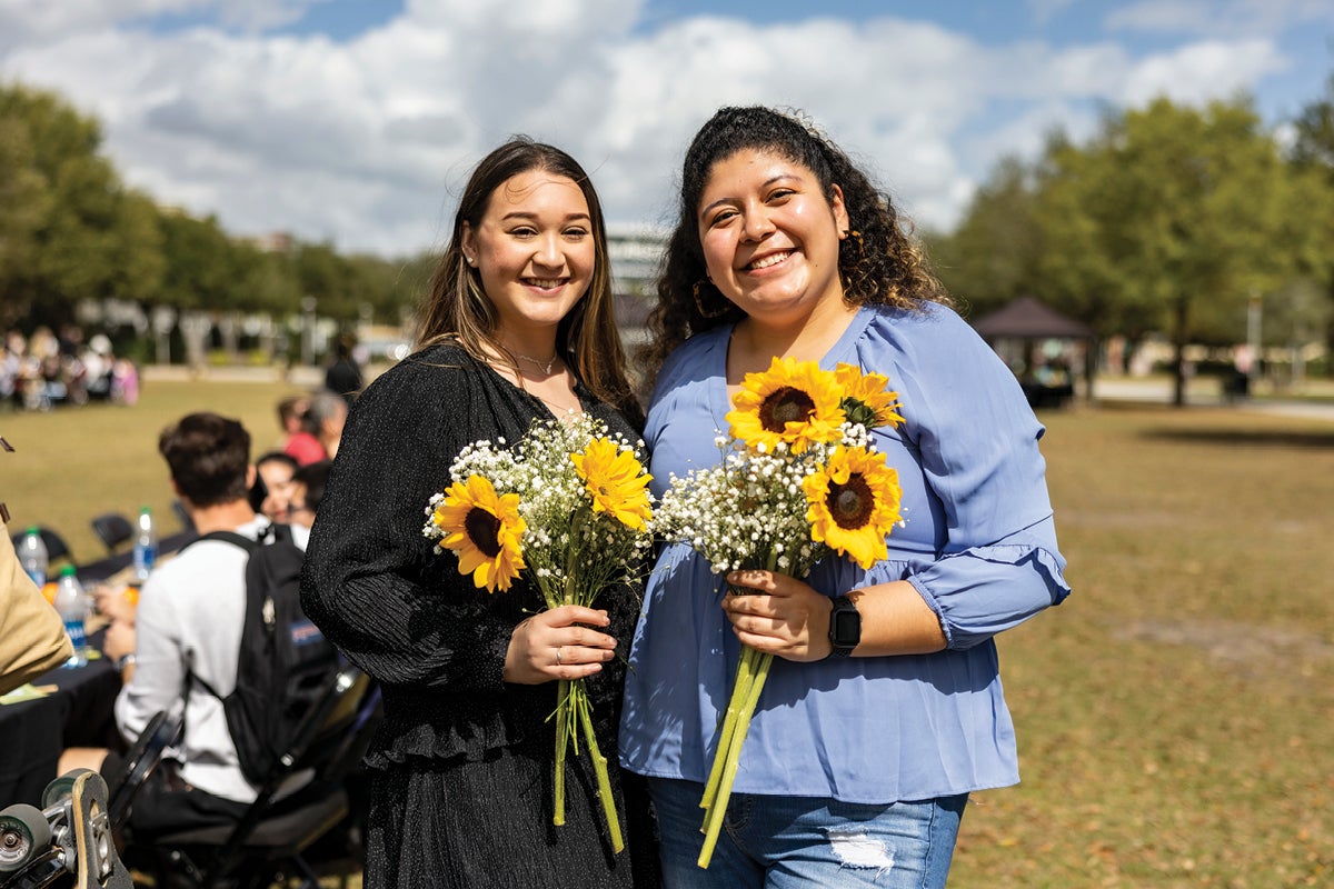 Two students smile while holding flowers.